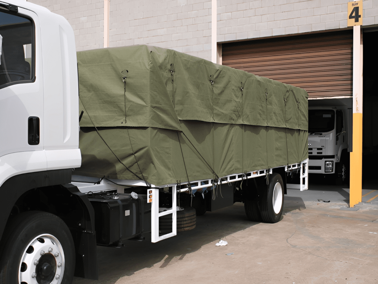 Truck with green tarpaulin parked outside warehouse.