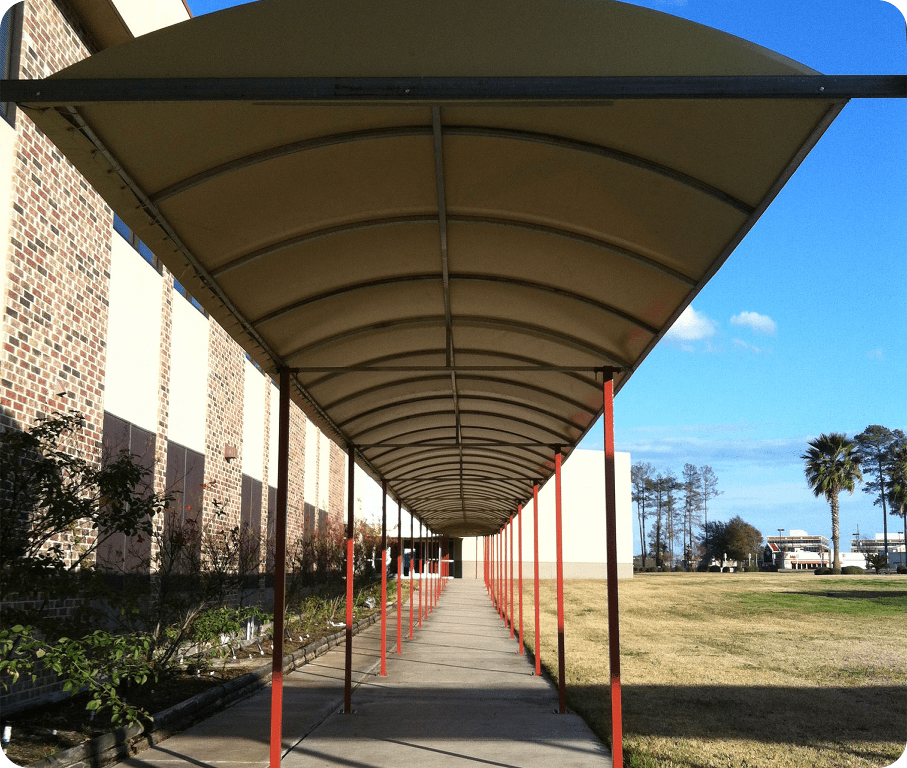 Covered walkway with red poles and trees.