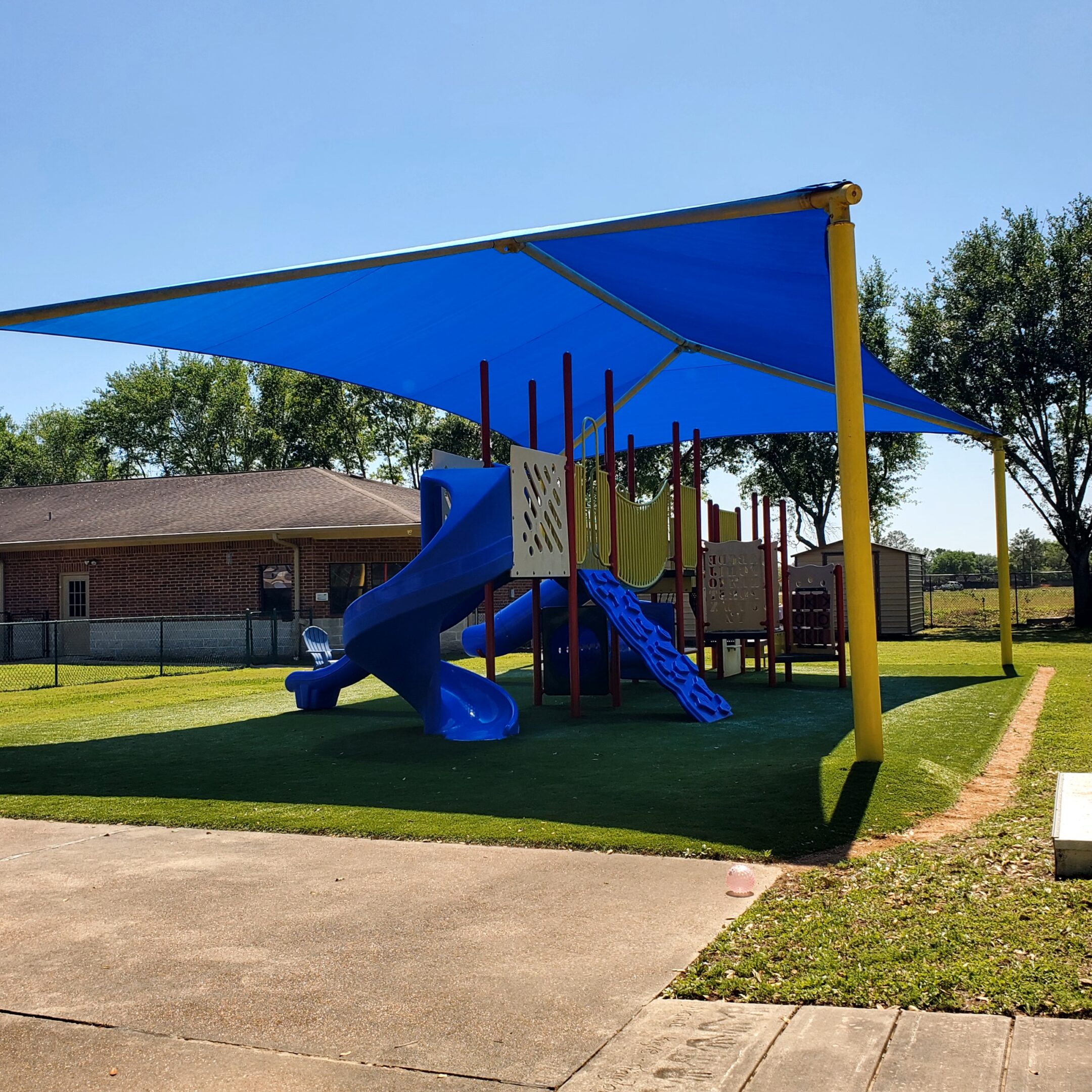 Playground with blue shade canopy and slide on artificial turf.