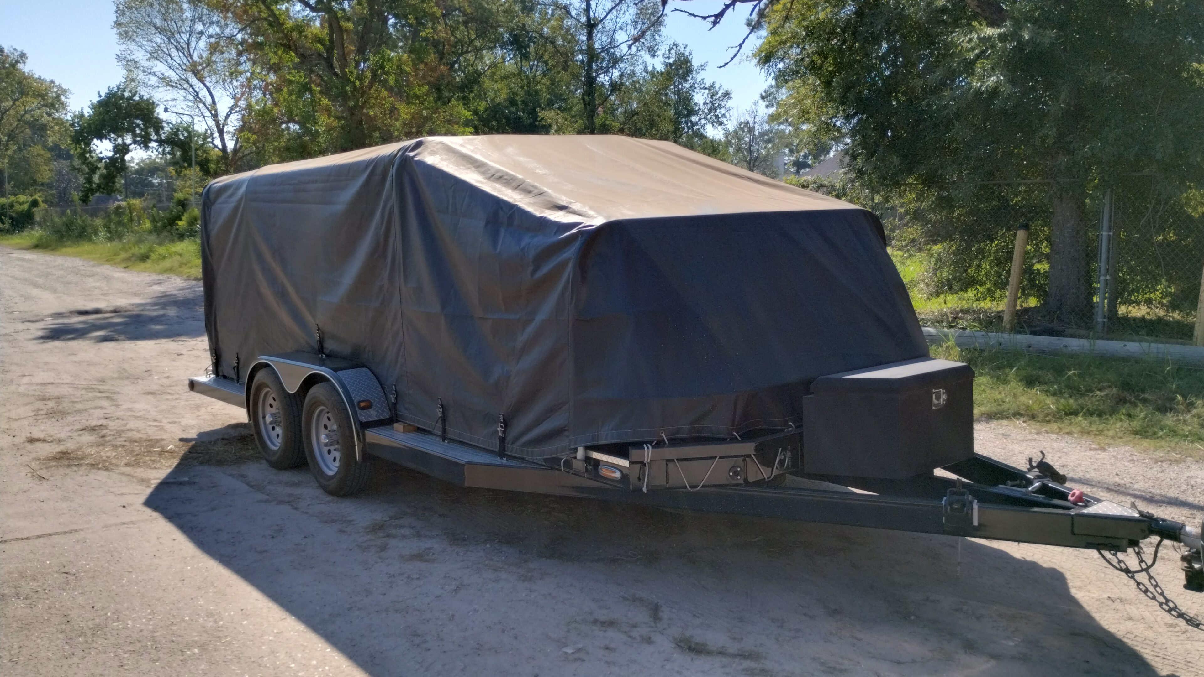 A covered utility trailer parked outdoors on a sunny day.