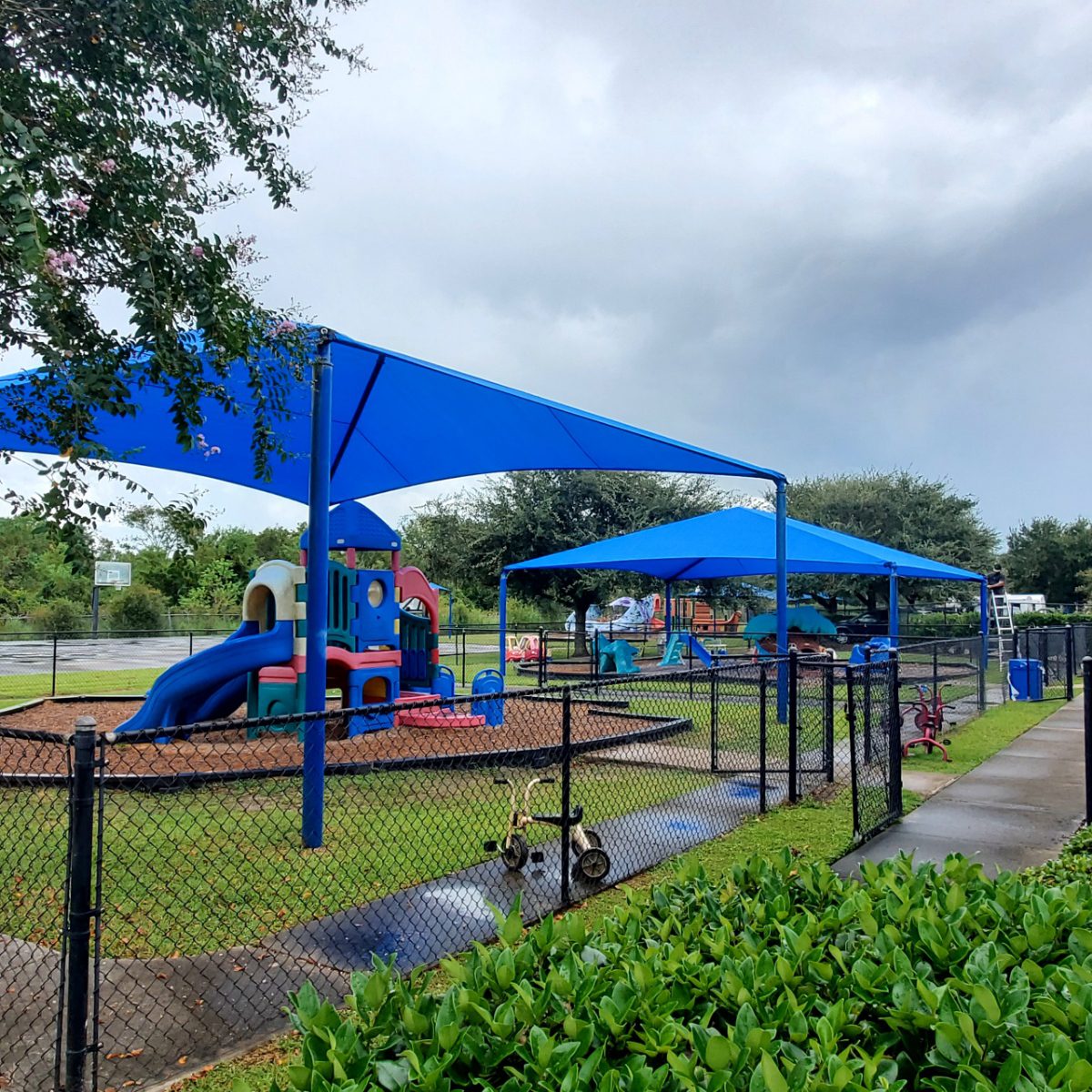 Playground with blue shade structures and slides on a cloudy day.